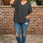 Woman wearing charcoal gray v-neck top standing in front of brick wall terrace