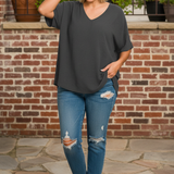 Woman wearing charcoal gray v-neck top standing in front of brick wall terrace