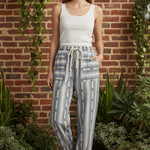 Model wearing cactus stripe jogger pants with white tank top in front of brick wall with greenery