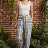 Model wearing cactus stripe jogger pants with white tank top in front of brick wall with greenery