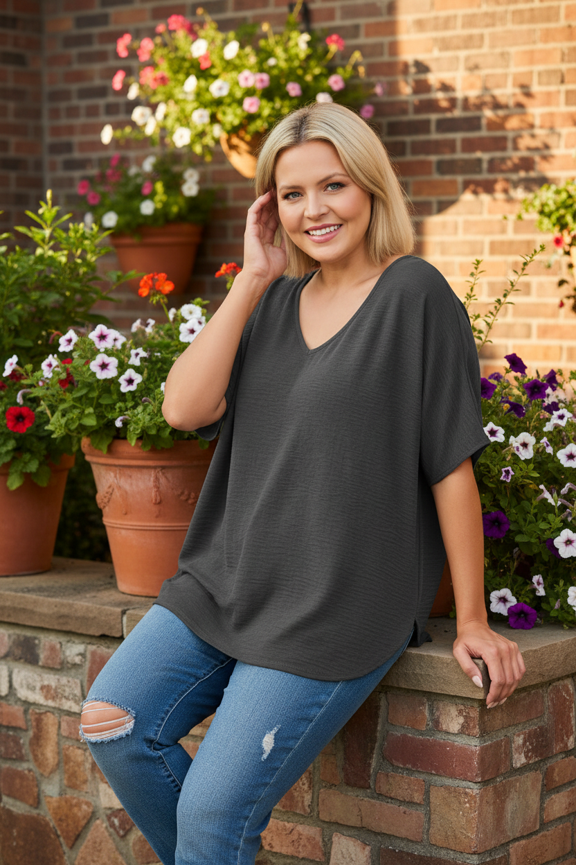 Woman sitting on terrace railing wearing charcoal gray v-neck top with brick wall background