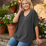Woman sitting on terrace railing wearing charcoal gray v-neck top with brick wall background