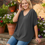 Woman sitting on terrace railing wearing charcoal gray v-neck top with brick wall background