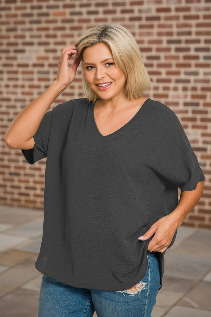 Woman wearing a dark gray oversized shirt and blue jeans against a brick wall.