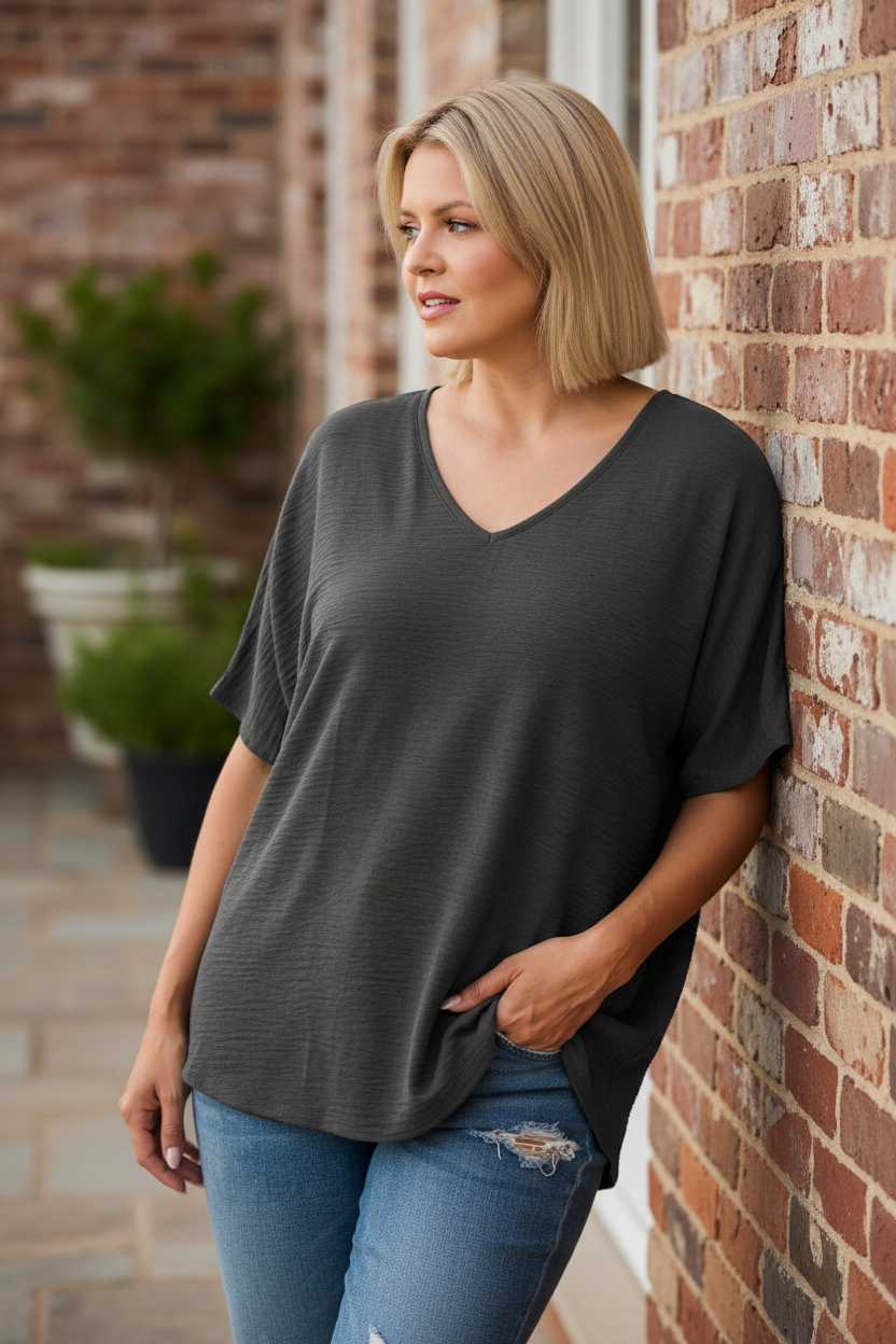 Woman leaning against brick wall wearing charcoal gray v-neck top on terrace