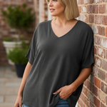 Woman leaning against brick wall wearing charcoal gray v-neck top on terrace