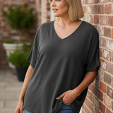 Woman leaning against brick wall wearing charcoal gray v-neck top on terrace