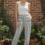 Model wearing cactus stripe jogger pants with white tank top in front of brick wall with greenery