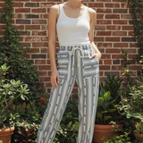 Model wearing cactus stripe jogger pants with white tank top in front of brick wall with greenery