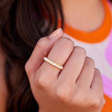 Close-up of a hand wearing a gold ring with a colorful background