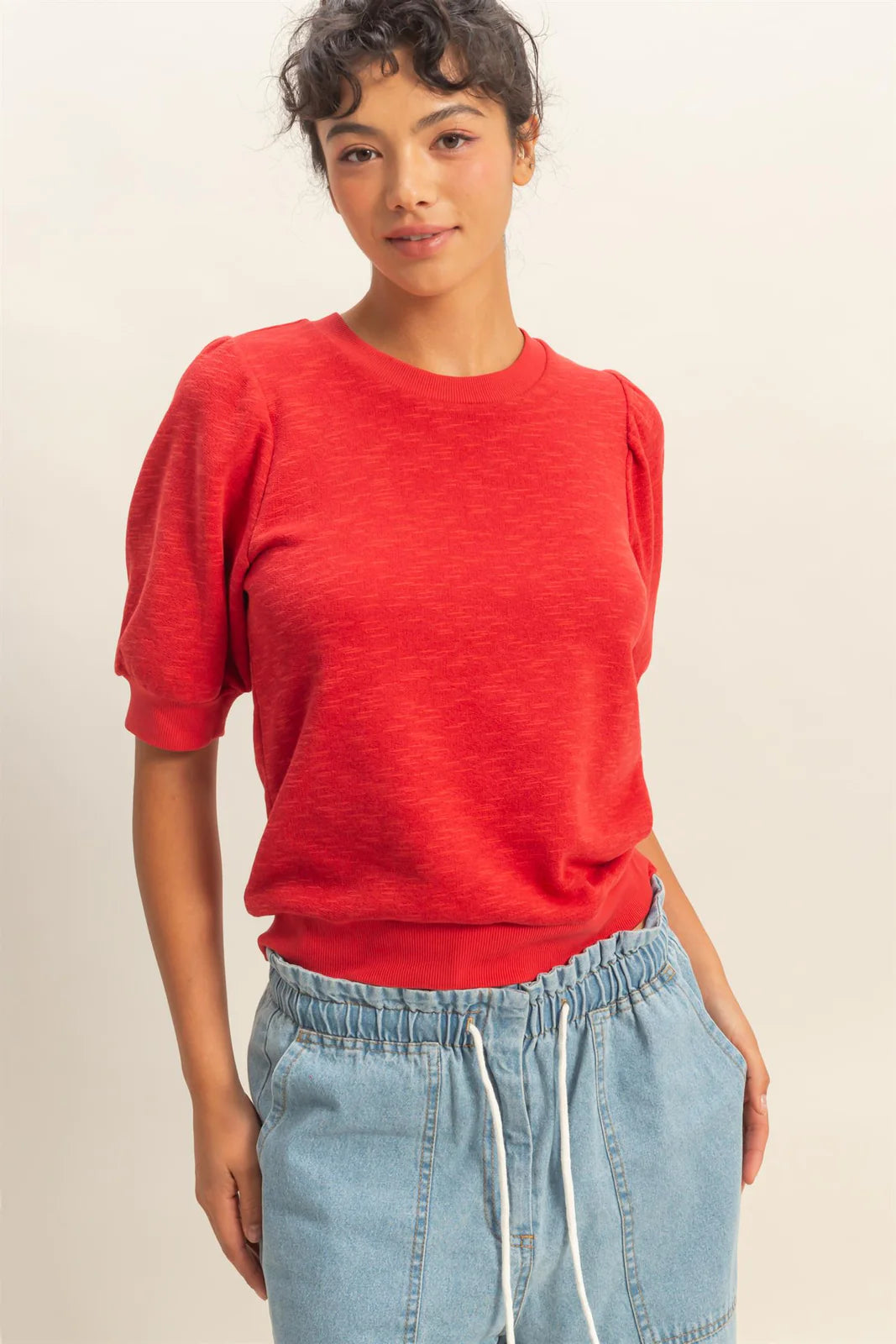 Person wearing a red shirt and blue jeans on a plain background