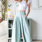 Woman wearing a white crop top and light green wide-leg pants in a bright room.