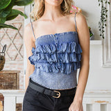 Woman wearing a blue ruffled top and black shorts in an indoor setting with plants.
