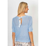 Woman wearing a light blue knit top with a ribbon detail on a white background