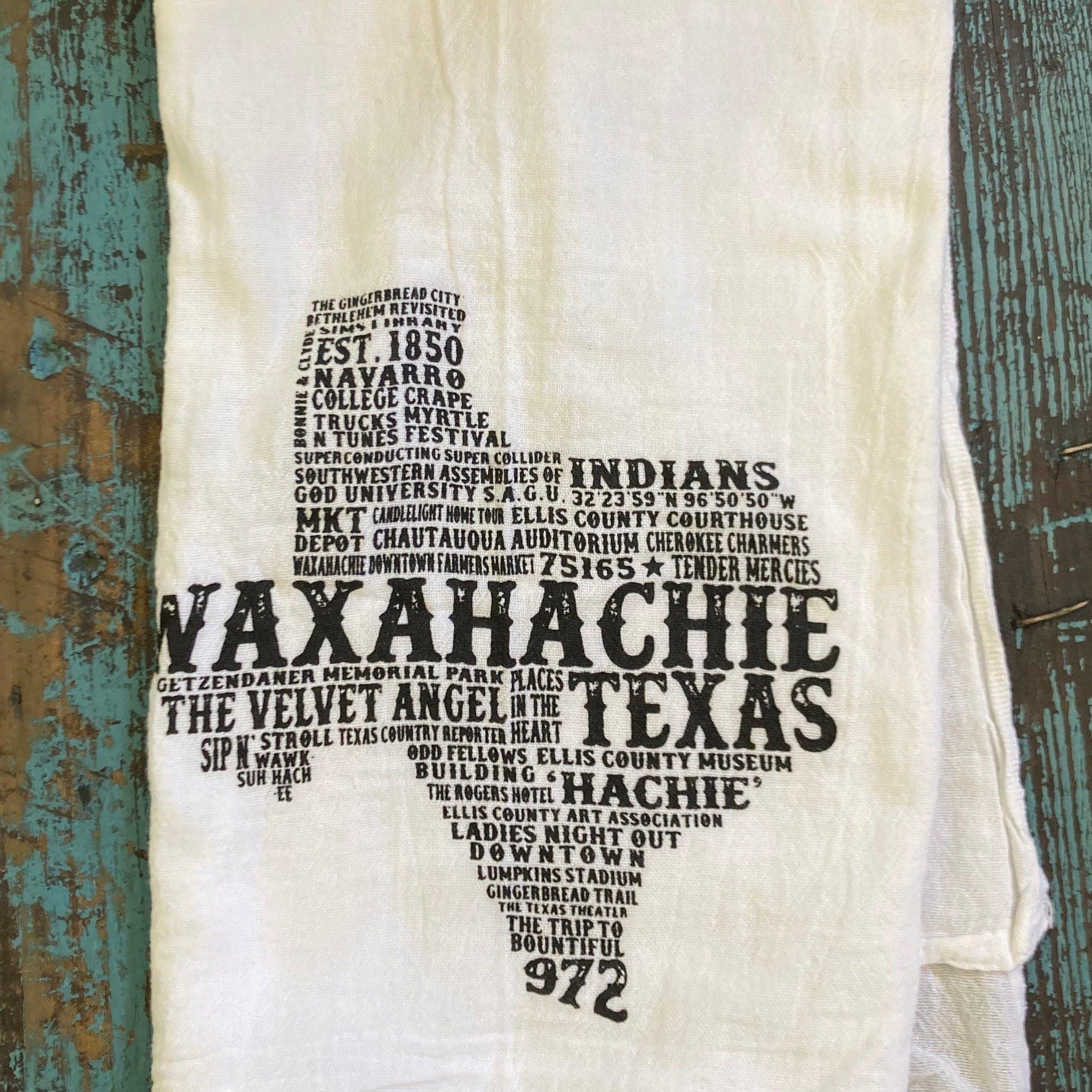 White towel with black text about Waxahachie, Texas, on a wooden background