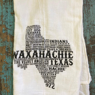 White towel with black text about Waxahachie, Texas, on a wooden background